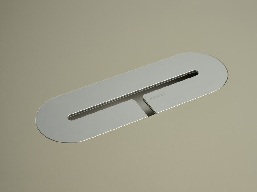 An anodised aluminum oval cable lid by Daniel Lorch. It sits on its tabletop cut-out hole, effectively organising cables, and protecting them from abrasion.