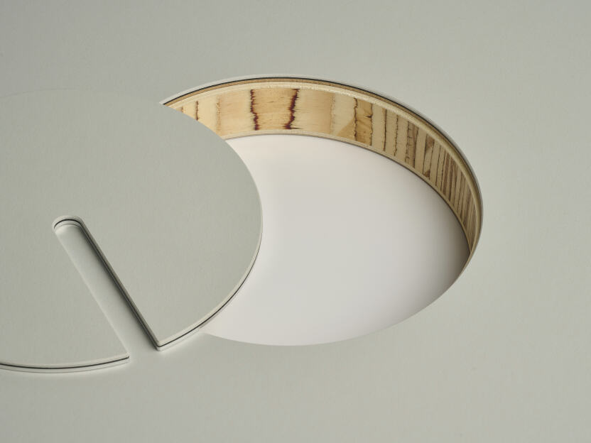 An anodised aluminum round cable lid by Daniel Lorch, covered with Vapoor linoleum on one side. It sits next to its tabletop cut-out hole, revealing the Laminboard tabletop core material.