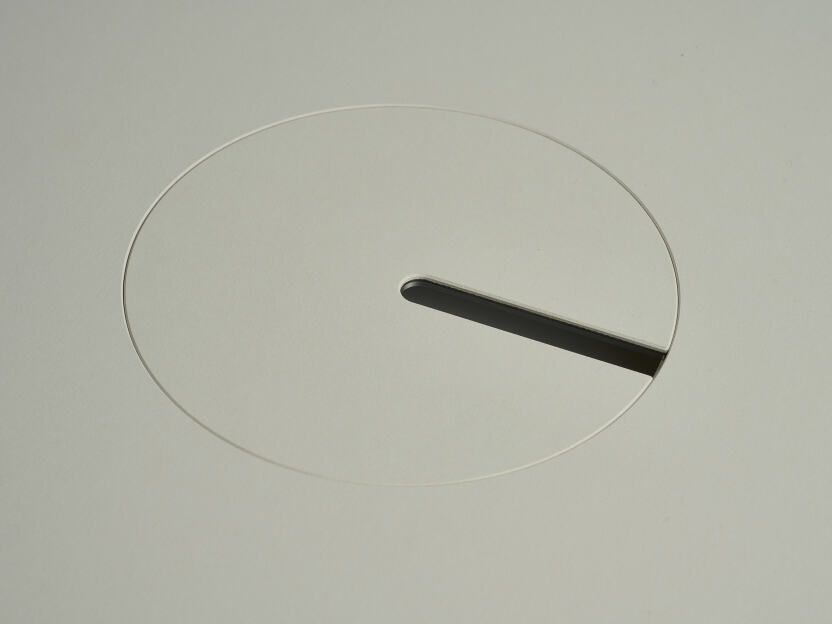 An anodised aluminum round cable lid by Daniel Lorch, covered with Vapoor linoleum on one side. It sits on its tabletop cut-out hole, effectively organising cables, and protecting them from abrasion.