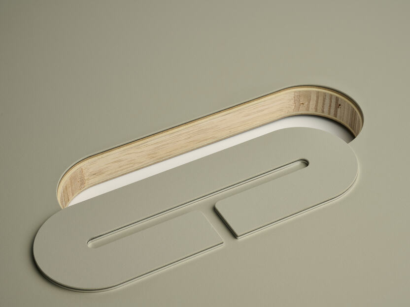 Eine eloxierte Aluminium-Ovalabdeckung für Kabel von Daniel Lorch, die auf einer Seite mit Vapoor-Linoleum bedeckt ist. Sie liegt neben der Aussparung der Tischplatte und offenbart das Laminboard der Tischplattenkernmaterialien.
