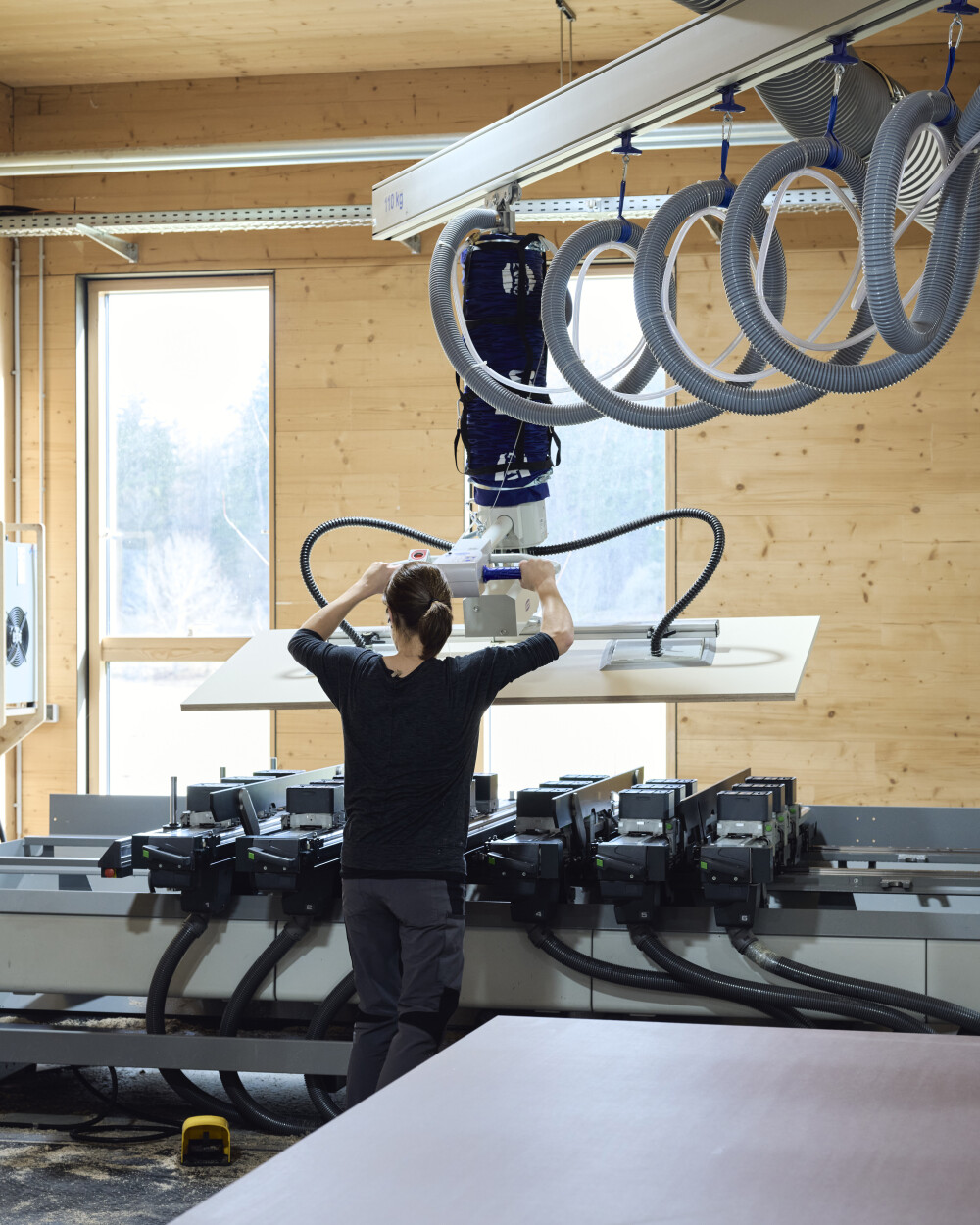 Person arbeitet in einer modernen Werkstatt an einer CNC-Maschine, auf der eine große Tischplatte bearbeitet wird.