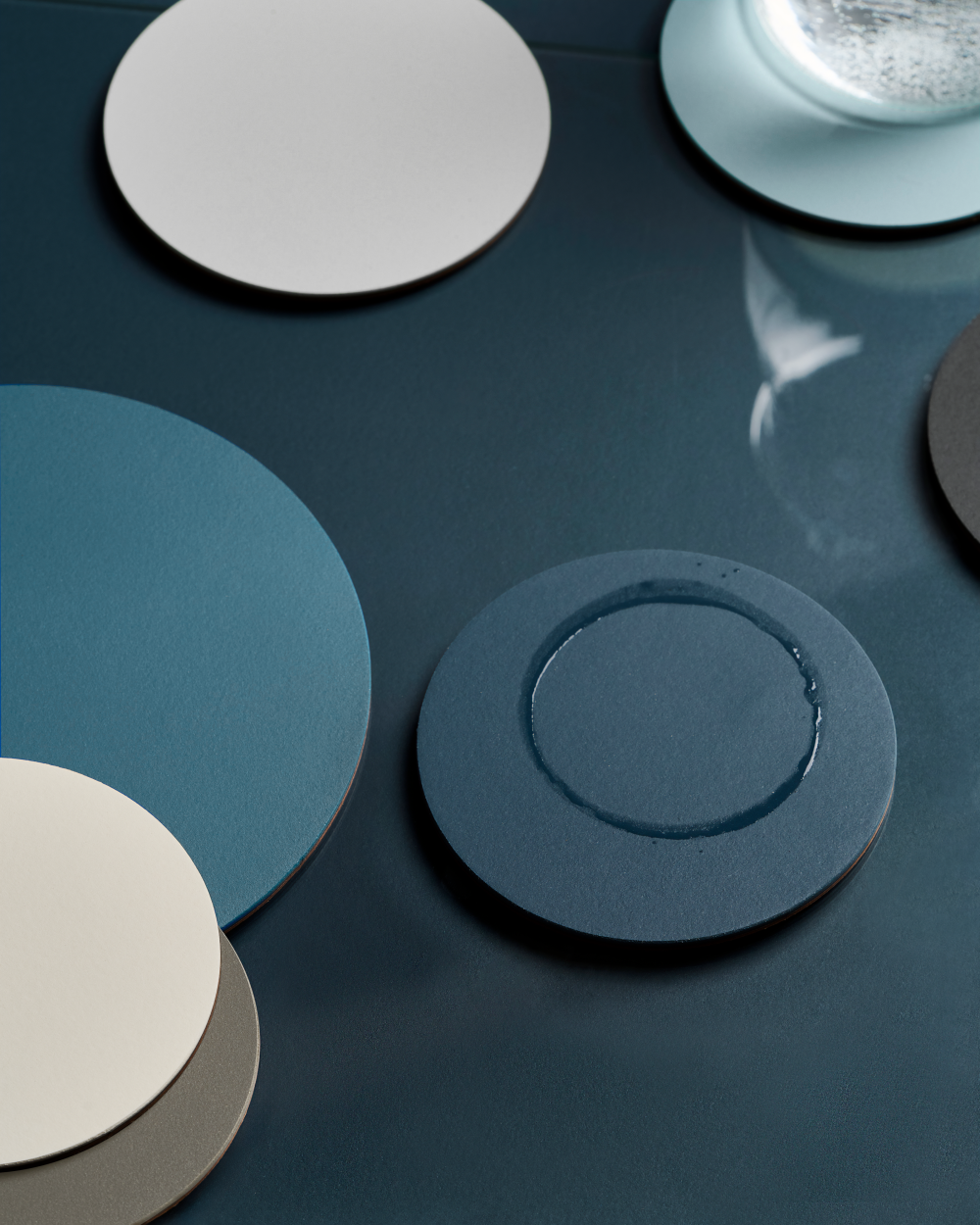 PAD Untersetzer aus Linoleum in kühlen Blautönen auf dunkellauer Linoleum Tsichplatte arrangiert.