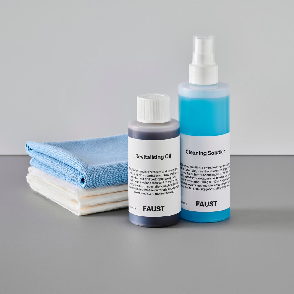Ein Set von Pflegeprodukten von Faust enthält revitalisierendes Öl und Reinigungslösung in halbtransparenten Flaschen mit Markenlabels. Im Hintergrund drei weiße Baumwolltücher und ein hellblaues Mikrofasertuch.