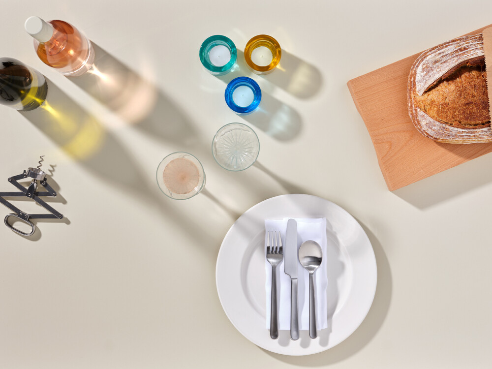 Linoleum-Tischplatte in warmem Beige (Mushroom) mit gedecktem Arrangement aus Brot, Glas, Besteck und Wein – inszeniert als Esstischszene.