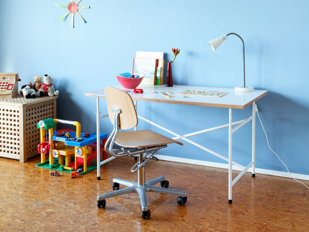 E2 Kinder-Schreibtisch mit weißer Platte im Kinderzimmer, genutzt als Arbeitsplatz mit Lampe, Büchern und Spielzeug.