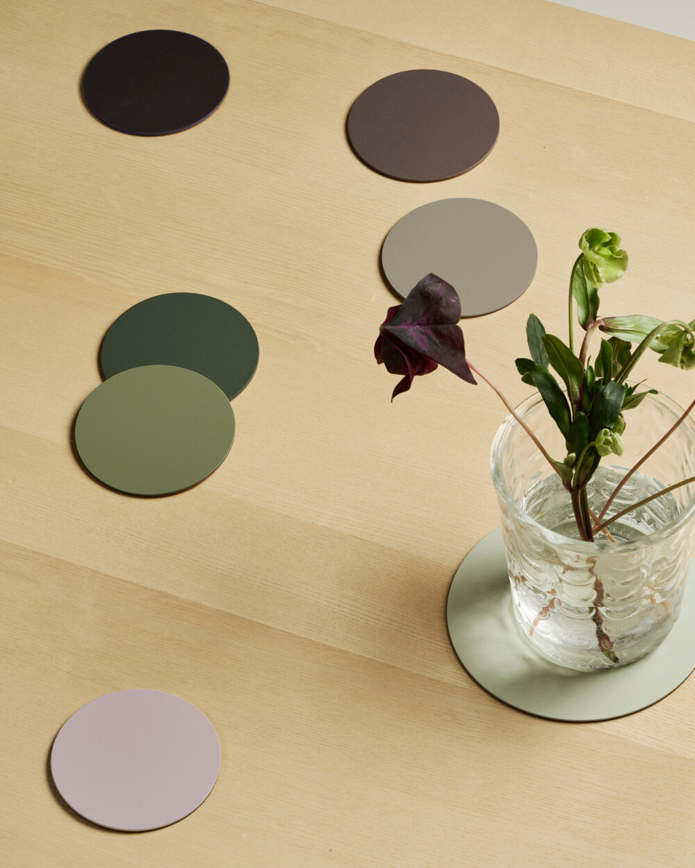 PAD Untersetzer aus Linoleum in verschiedenen Farben der Kollektion Wildwood, arrangiert auf hellem Holztisch  mit Glasvase.