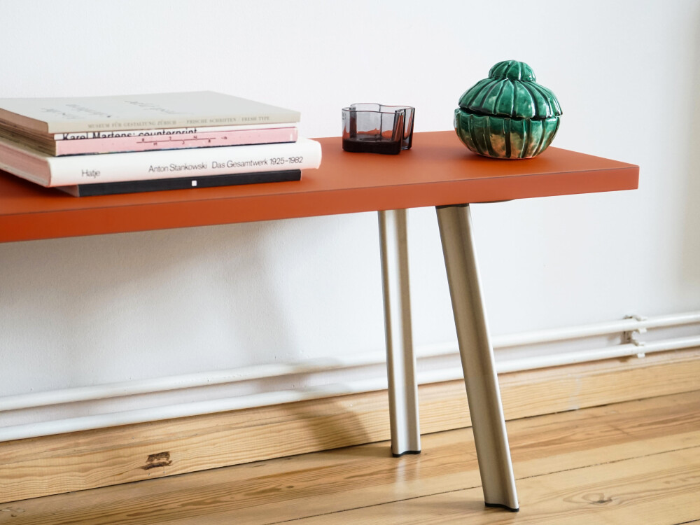 Detailansicht der BEAM Bank mit Backsteinfarbener Linoleumoberfläche und hellen Stahlbeinen, dekoriert mit Büchern.