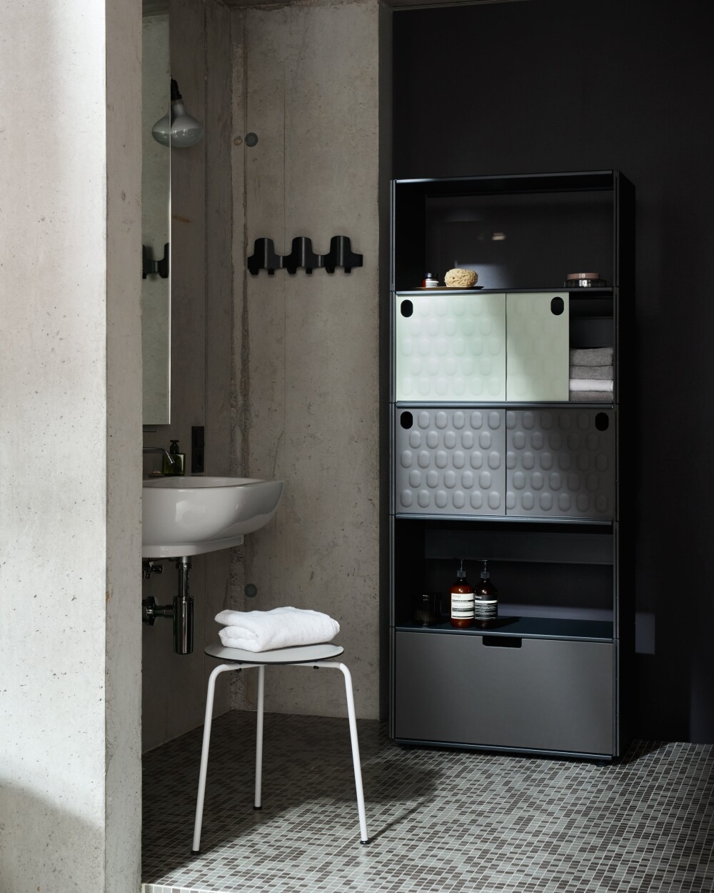 RAVIOLI Hocker mit Linoleum-Sitzfläche in Hellgrau in modernem Badezimmer mit Betonwänden und Regal.